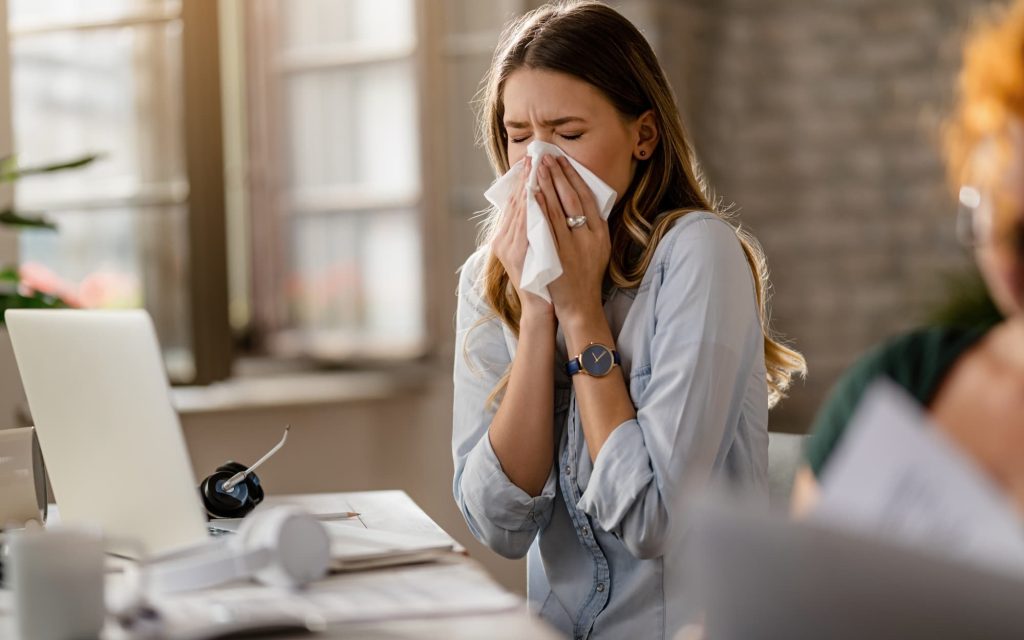 Woman sneezes into tissue at desk.